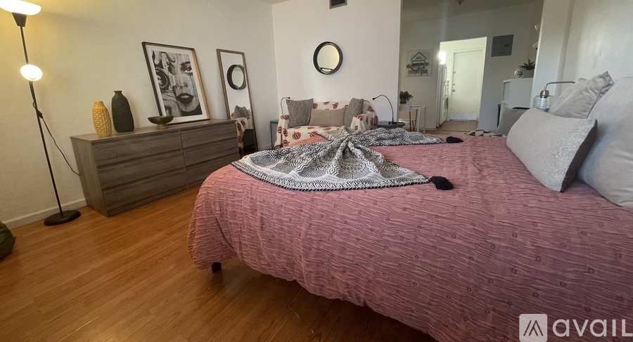 A bedroom with a pink bedspread and a wooden dresser.
