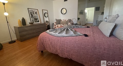 A bedroom with a pink bedspread and a wooden dresser.