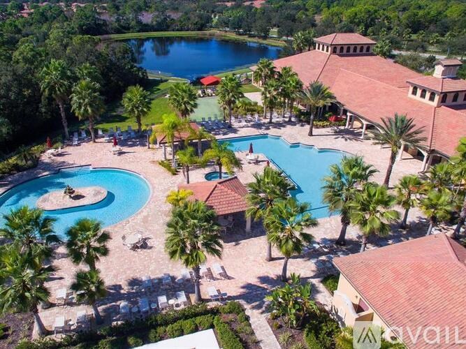 A large outdoor swimming pool surrounded by palm trees and a red-roofed building.