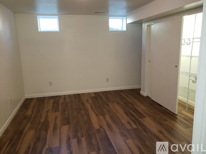 A room with wooden flooring and two windows.