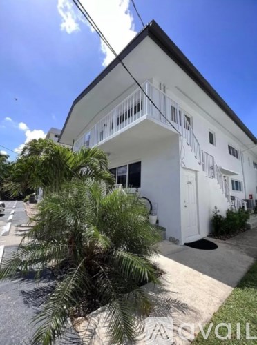 A white building with a balcony and a tree in front.