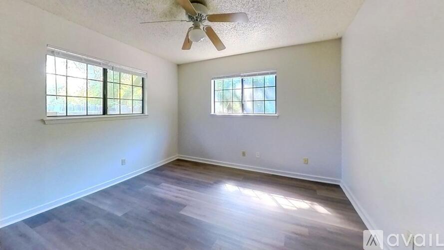 A room with a ceiling fan and two windows.