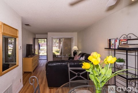 A living room with a black leather couch and a vase of yellow tulips on a glass table.