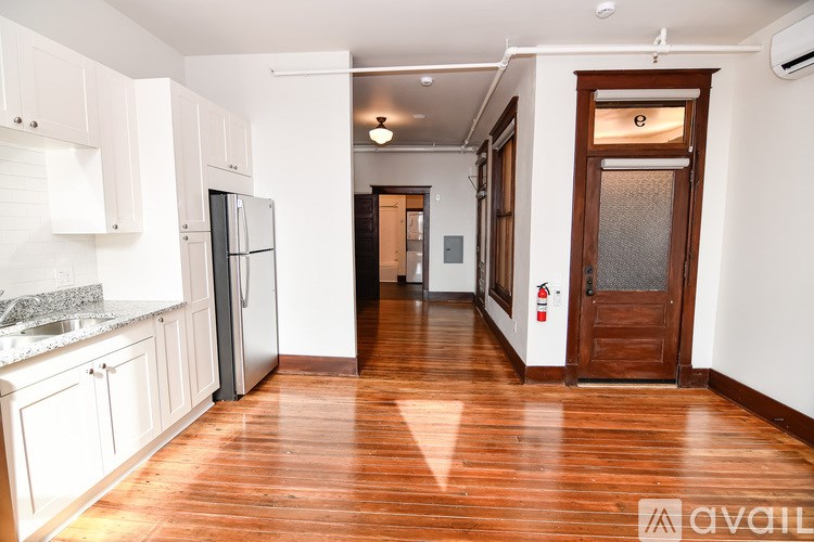 A kitchen with white cabinets and a wooden floor leading to a hallway.