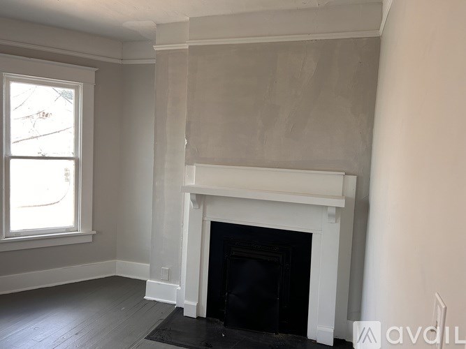 A white fireplace in a room with a window.