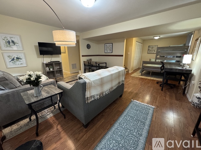 A living room with a grey couch, a coffee table, a bed with a white blanket, and a blue rug.