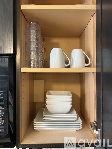 A kitchen cabinet with a microwave on the left and shelves with plates and cups.