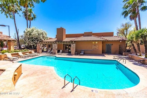 A large swimming pool in front of a house with a patio and palm trees.