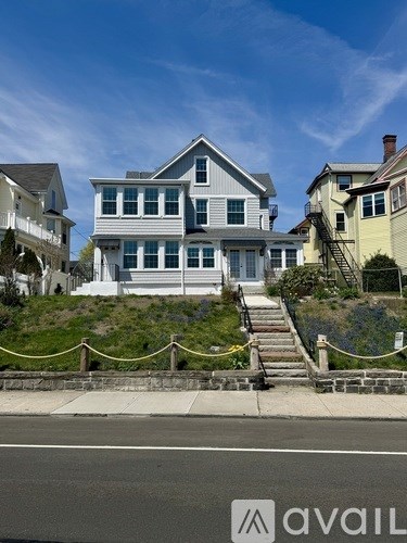 A house with a grey and white exterior is situated on a hill with a yellow rope barrier in front.