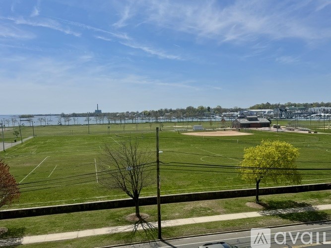 A view of a field with a fence and trees in the foreground and a building in the distance.
