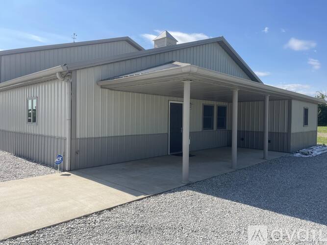 A grey building with a covered porch and a blue sign on the ground.