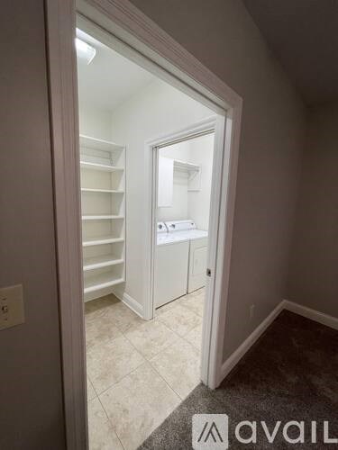 A white doorway opens to a kitchen with white cabinets and a tiled floor.