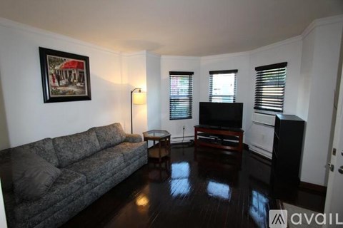 A living room with a grey couch, a small table, a television, and a painting on the wall.