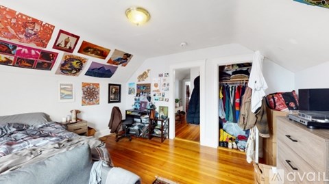 A bedroom with a bed, a chair, and a wall covered in pictures.