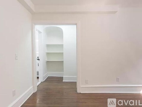 A room with a doorway leading to another room, a shelf, and a wooden floor.
