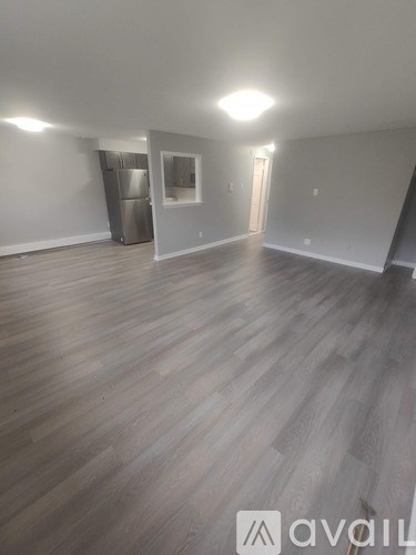 A spacious room with wooden flooring and a refrigerator in the corner.