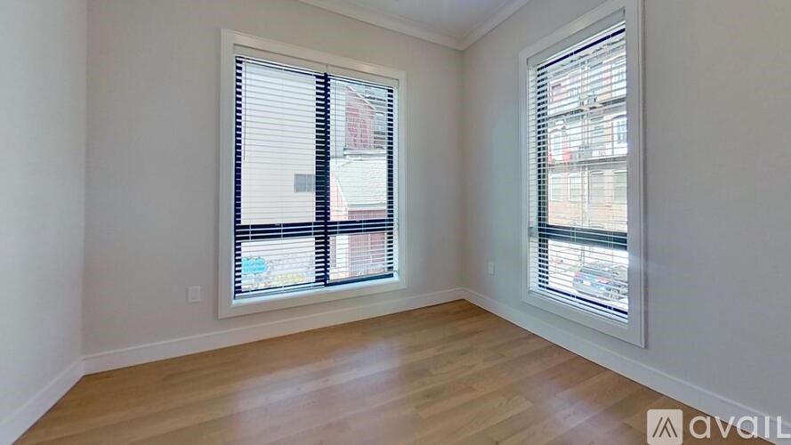 A room with wooden floors and two windows with blinds.