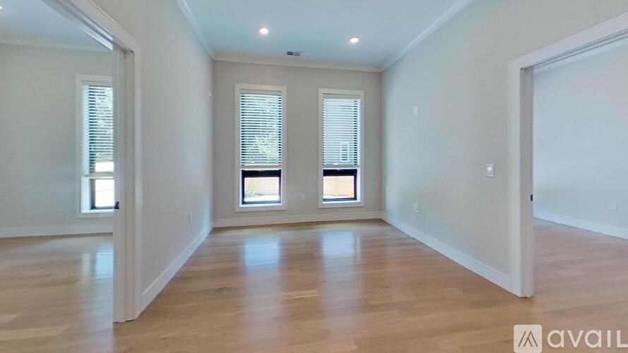 A spacious room with wooden floors and two windows with blinds.