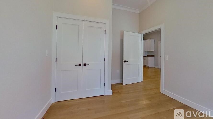 A room with white walls and wooden floors, featuring a white double door and a white single door.