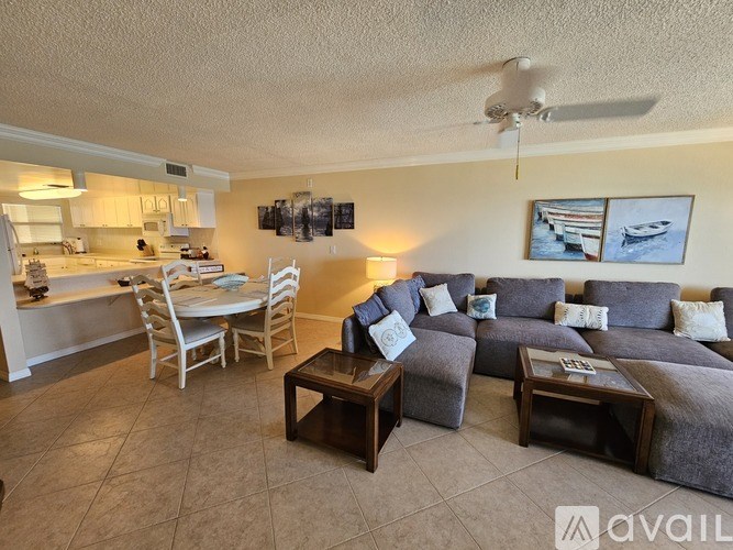 A living room with a grey couch, a dining table with chairs, and a ceiling fan.