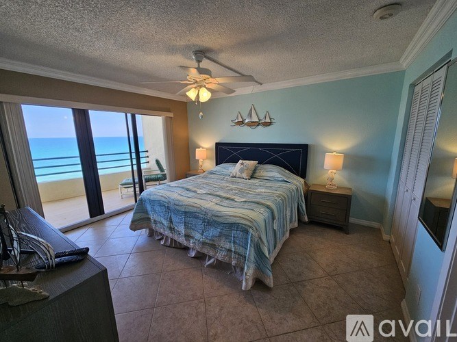 A bedroom with a bed, a ceiling fan, and a view of the beach.