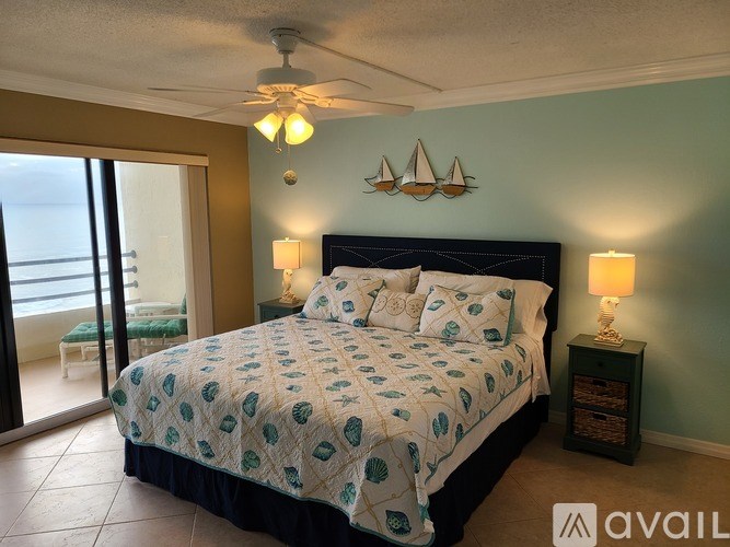 A bedroom with a bed, a ceiling fan, and a nightstand with a lamp.