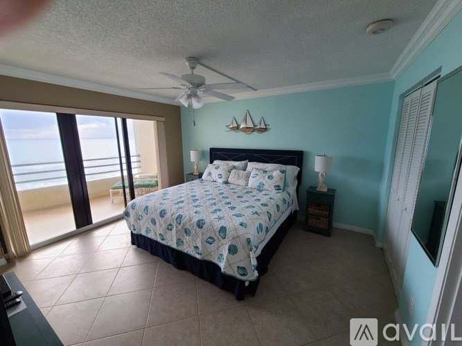 A bedroom with a bed, a ceiling fan, and a view of the ocean through the sliding glass doors.