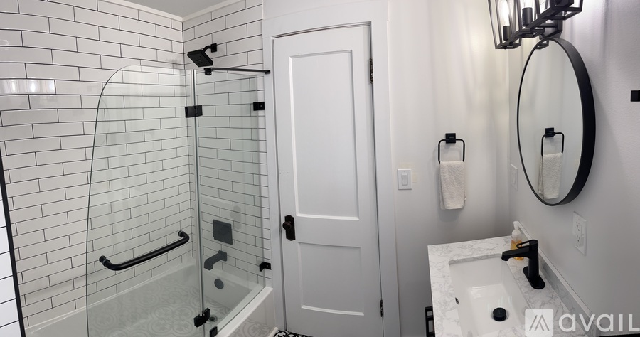 A bathroom with a white door, a round mirror, and a glass shower.