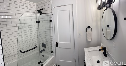 A bathroom with a white door, a round mirror, and a glass shower.