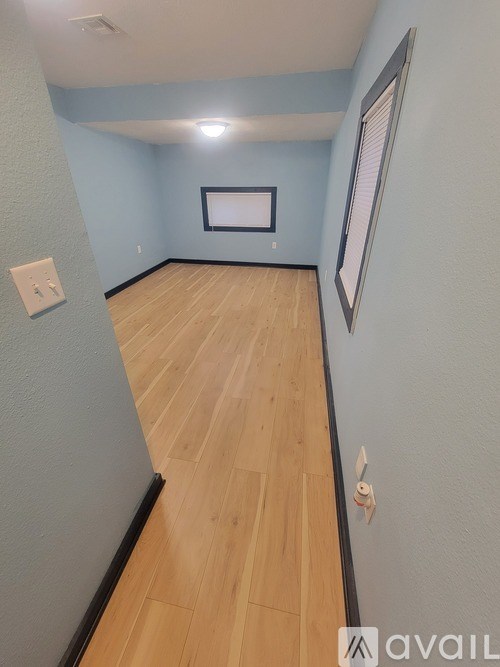 A long hallway with wood floors and a light switch on the wall.