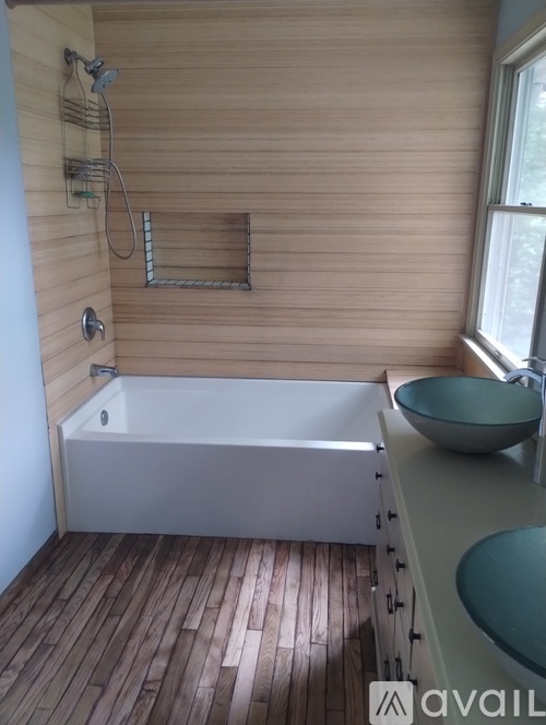 A bathroom with wooden floors and a white bathtub.