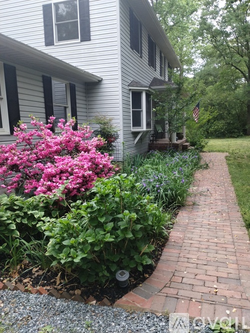 A brick pathway leads to a house with a flag on the front porch.
