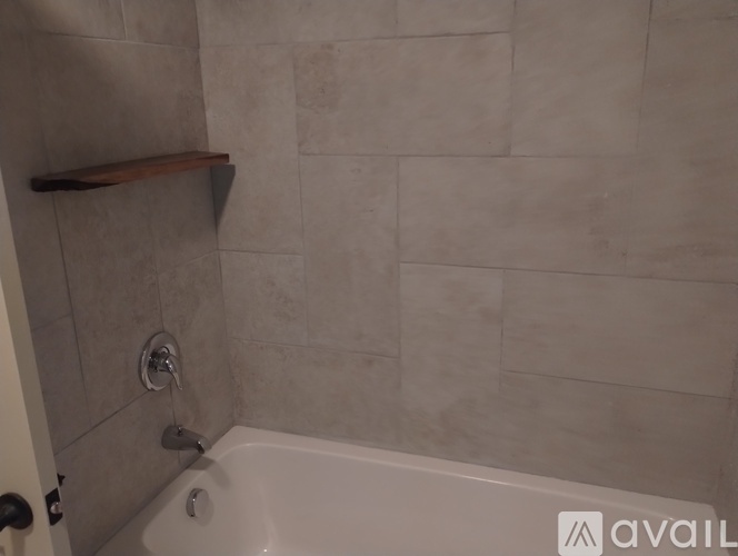 A bathroom with a white tub and a wooden shelf above it.