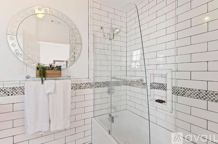 A bathroom with a white tiled shower and a round mirror above a towel rack.