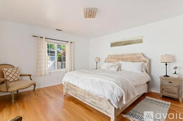 A bedroom with a large bed, a chair, and a window.