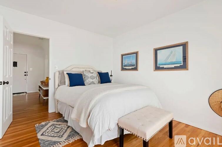 A bedroom with a bed, a bench, and two pictures on the wall.