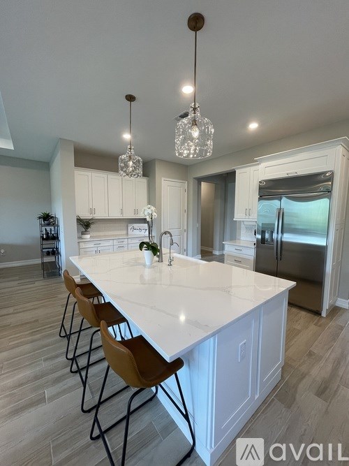 A kitchen with a long white island and wooden chairs.