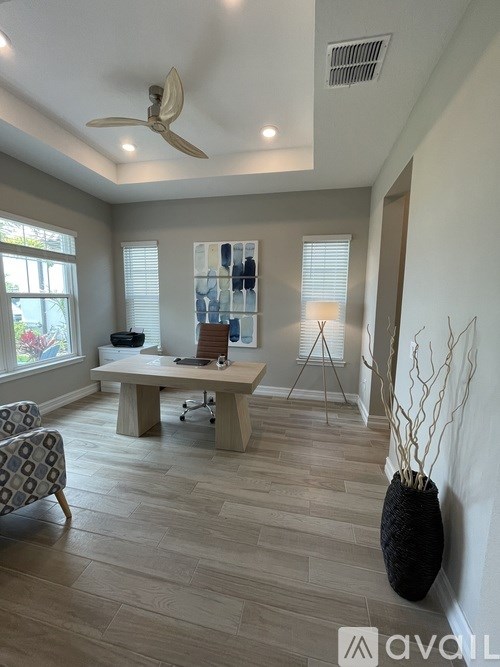 A room with a ceiling fan, a desk with a chair, and a vase on the floor.