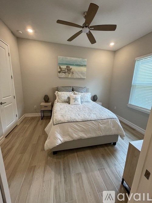 A bedroom with a bed, a ceiling fan, and a painting on the wall.