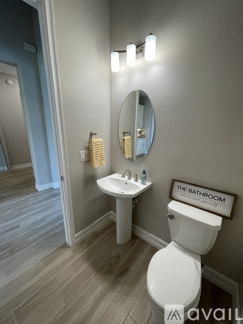 A bathroom with a toilet, sink, mirror, and light fixture.