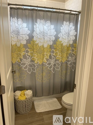 A bathroom with a floral shower curtain and a basket of towels.