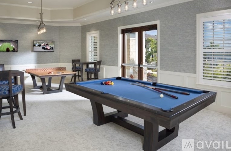 A pool table is in the middle of a room with a television and a window.