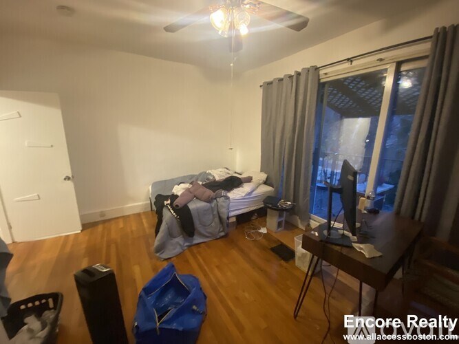 A room with a bed, a table, and a ceiling fan.