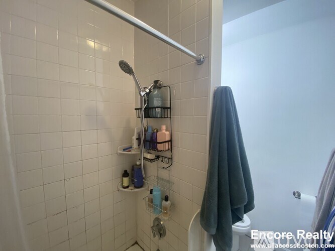 A white tiled shower with a shelf and a shower head.