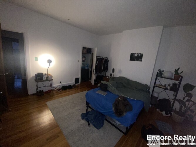 A room with a bed, a chair, and a table with a lamp on it.