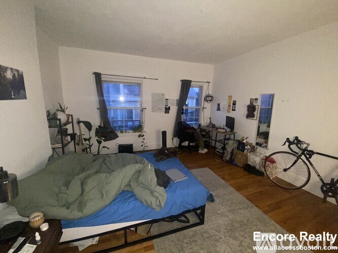 A bedroom with a bed, a desk, a chair, a bicycle, and a window.