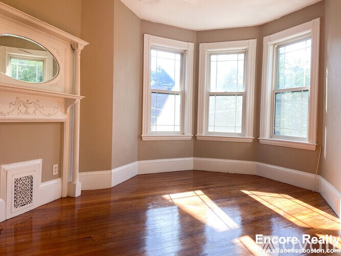 A sunlit room with a fireplace and three windows.