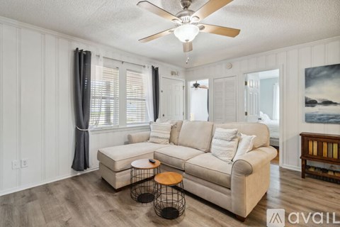 A living room with a beige couch, a ceiling fan, and a painting of a beach scene on the wall.