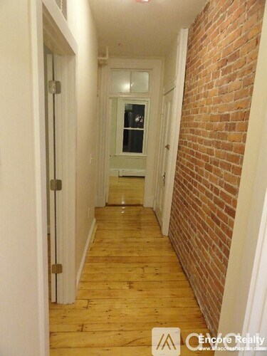 A long hallway with a brick wall on the side and a white door at the end.