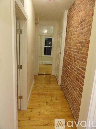 A hallway with a wooden floor and a brick wall.